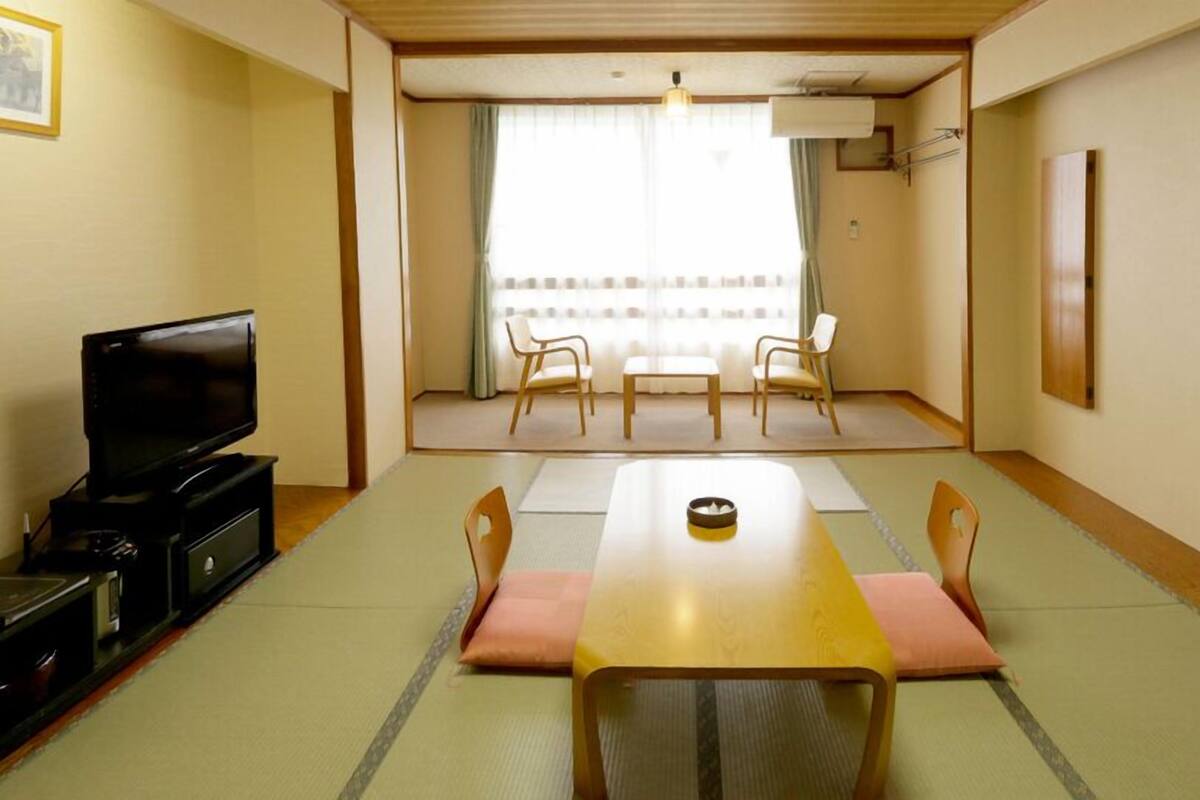 A room with tatami mats, a television, a table, and chairs.