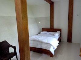 Quarto com cama de madeira, roupa de cama branca e uma única cadeira.