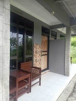 Uma área de estar coberta ao ar livre, com um banco e uma mesa, uma parede de pedra e uma porta com acabamento em madeira.