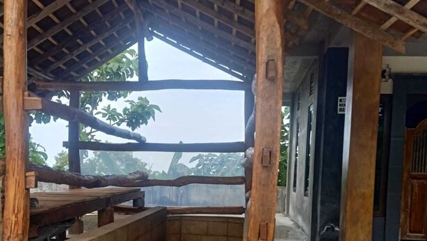 Un espacio al aire libre cubierto con estructura de madera, escalones de piedra y vistas a follaje.