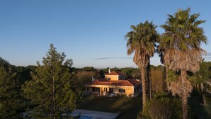 Una grande casa con tetto rosso, circondata da alberi e una piscina.