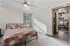 Un dormitorio con cama, ventilador de techo, ventana y vista a un comedor.