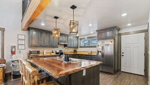 Una cocina con una isla central, taburetes de madera, electrodomésticos de acero inoxidable e iluminación colgante.