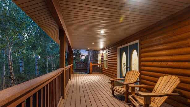 Une terrasse en bois avec deux fauteuils Adirondack, une rambarde en bois et une vue sur la forêt environnante.