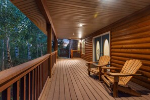 Une terrasse en bois avec deux fauteuils Adirondack, une rambarde en bois et une vue sur la forêt environnante.