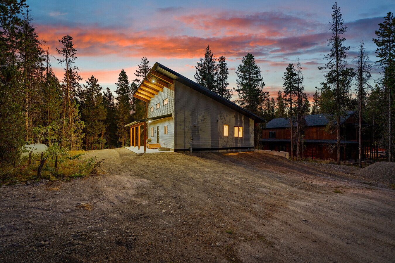 A modern two-story house with a sloped roof, surrounded by a forested area.