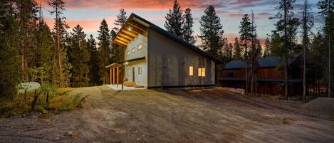 A modern two-story house with a sloped roof, surrounded by a forested area.