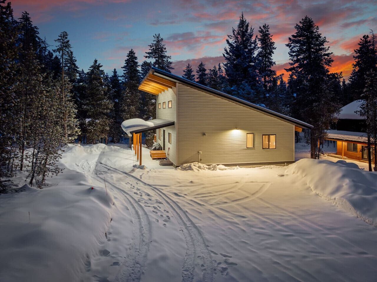 Una cabaña con techo inclinado, un porche y un paisaje cubierto de nieve.