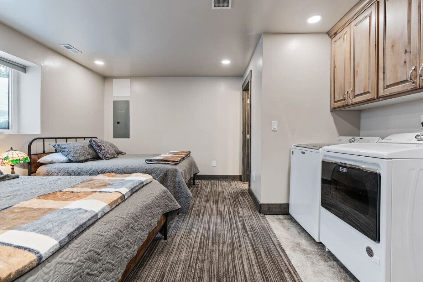 A small, compact room with two beds, a washing machine, and a window.