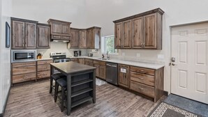 A spacious kitchen with wooden cabinets, a central island, and a built-in oven. - Prism Peaks | Hot Tub, Fire Pit, AC, Yellowstone, ATV, Views! (Island Park)