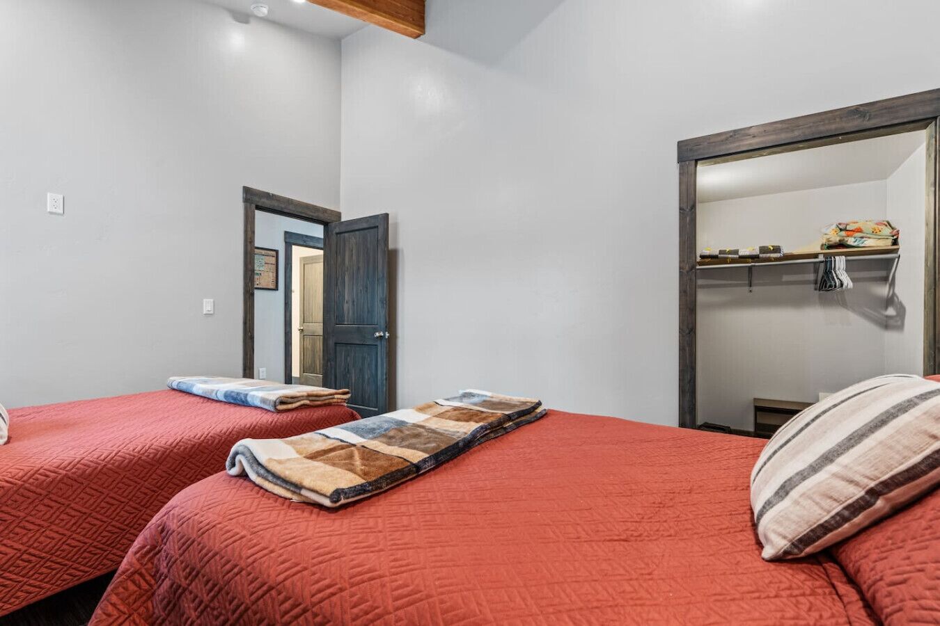 Una habitación con dos camas, cada una con un edredón rojo, una puerta de madera y un espejo en la pared.