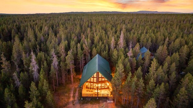 Eine Lodge mit einem großen zentralen Raum und einem kleineren Raum zur Rechten, umgeben von dichtem Wald.