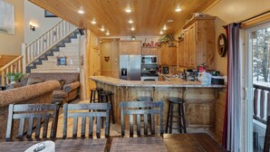 Ein gemütliches Blockhauss-Interieur mit einer Holztreppe, einer Küche mit Holzausstattung und einer Bar mit Hockern.