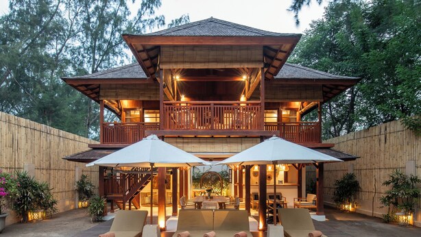 A two-story wooden house with a balcony, a pool, and outdoor furniture.