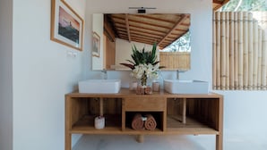 A wooden vanity with two sinks, a mirror, and a vase with flowers.