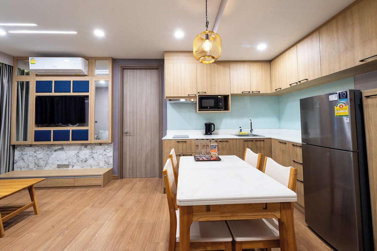 A compact kitchen with wooden cabinets, a stainless steel refrigerator, a microwave, and a dining table with chairs.