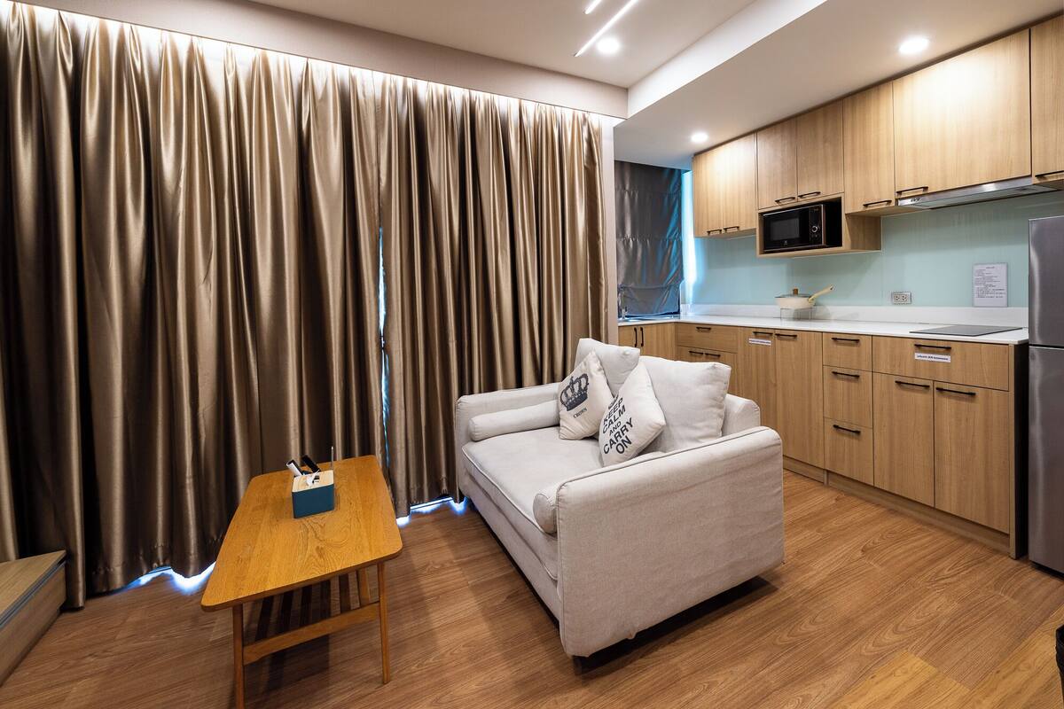 A modern living room with a sofa, a small wooden table, and a kitchen area with wooden cabinets and appliances.