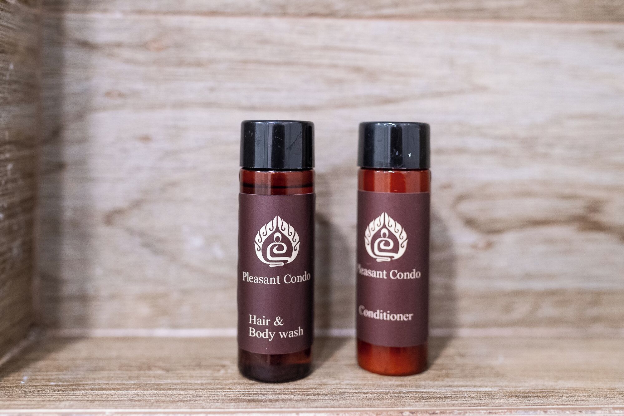 Two bottles of Pleasant Condo hair and body wash and conditioner on a wooden shelf.