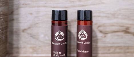 Two bottles of Pleasant Condo hair and body wash and conditioner on a wooden shelf.