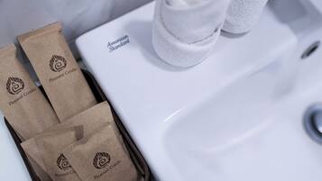 A bathroom sink with two white towels and three brown paper bags with the 'Pleasant Condo' logo.