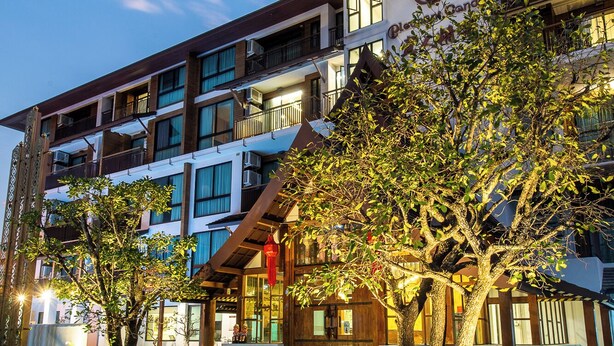 A multi-story building with a prominent logo, balconies, and a well-lit entrance area with trees. - Pleasant Chiangmai (Chiang Mai)