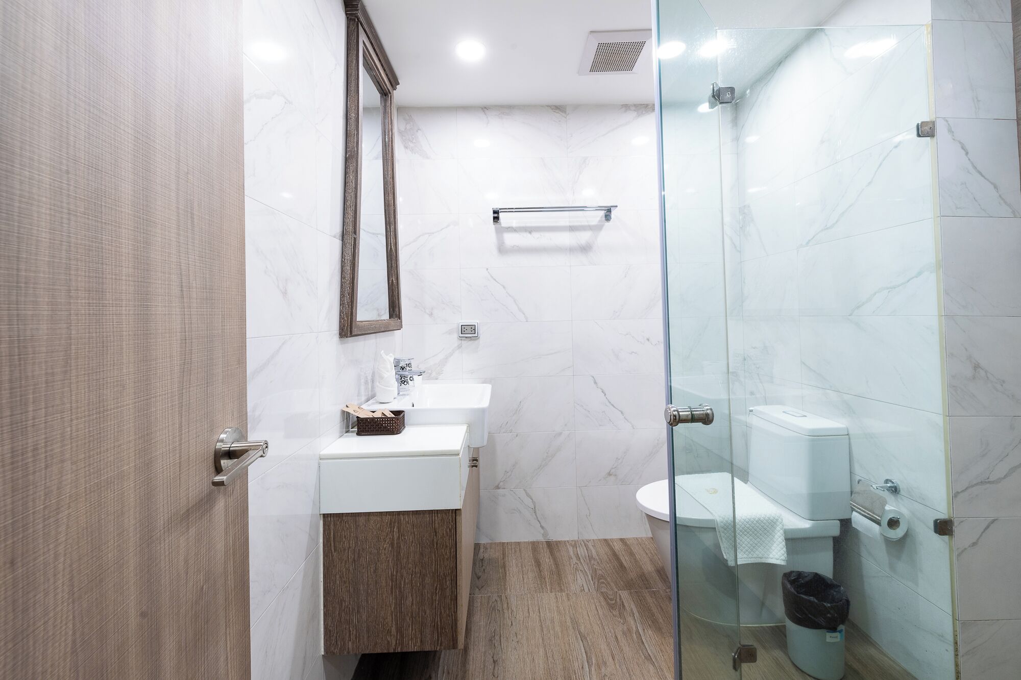A modern bathroom with a glass shower enclosure, a white sink, and a wooden vanity.