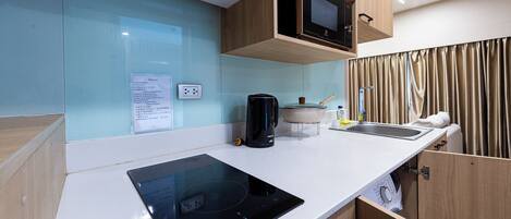 Una kitchenette compacta con estufa integrada, microondas y un lavamanos pequeño.