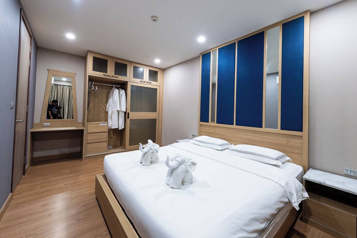 A hotel room with a wooden bed, a wardrobe with a mirror, and a large window with blue panels.