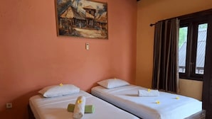 A room with two beds, each with white linens and a rolled towel. There is a painting on the wall above the beds, and a window with curtains to the right. - Brown Sugar Homestay (Gili Trawangan)