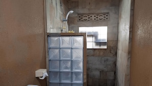 A compact bathroom with a toilet, a shower enclosure, and a small window. - Brown Sugar Homestay (Gili Trawangan)