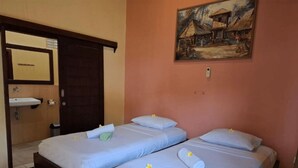 A room with two beds, each with a pillow and a rolled towel. There is a painting on the wall and a door to the left. - Brown Sugar Homestay (Gili Trawangan)