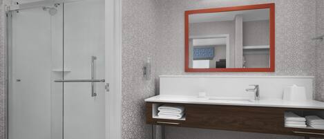 Un baño moderno con cabina de ducha de vidrio, tocador blanco con base de madera y espejo con marco rojo.