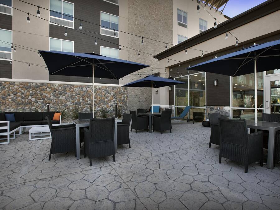Un espacio de patio al aire libre con suelo de piedra hexagonal, mobiliario de mimbre negro y sombrillas azules.