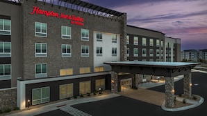 Een gebouw van Hampton Inn & Suites by Hilton met een modern ontwerp, gevel van baksteen, grote ramen en een overdekt entreegebied.