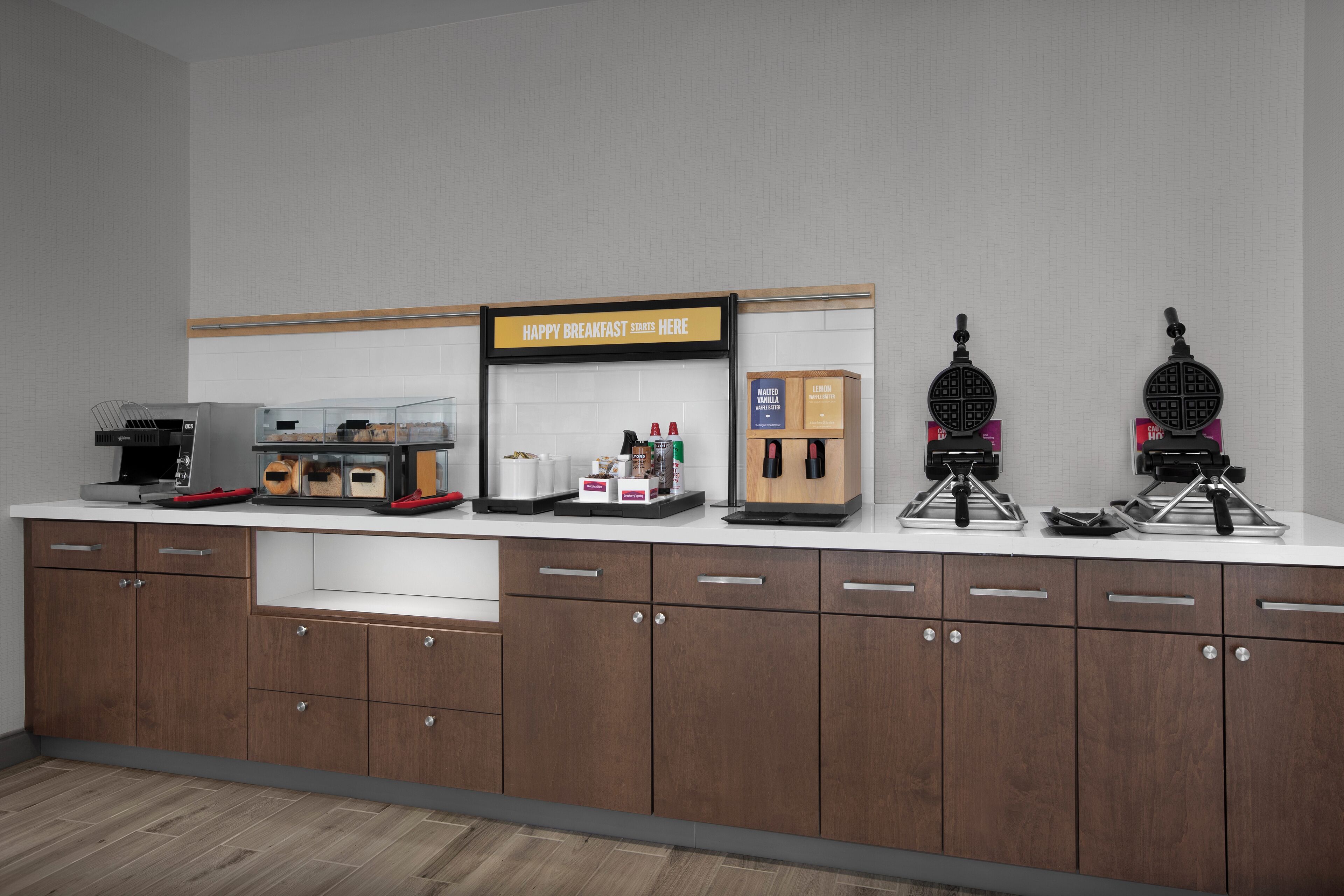 A breakfast bar with a sign, waffle makers, and a coffee machine.