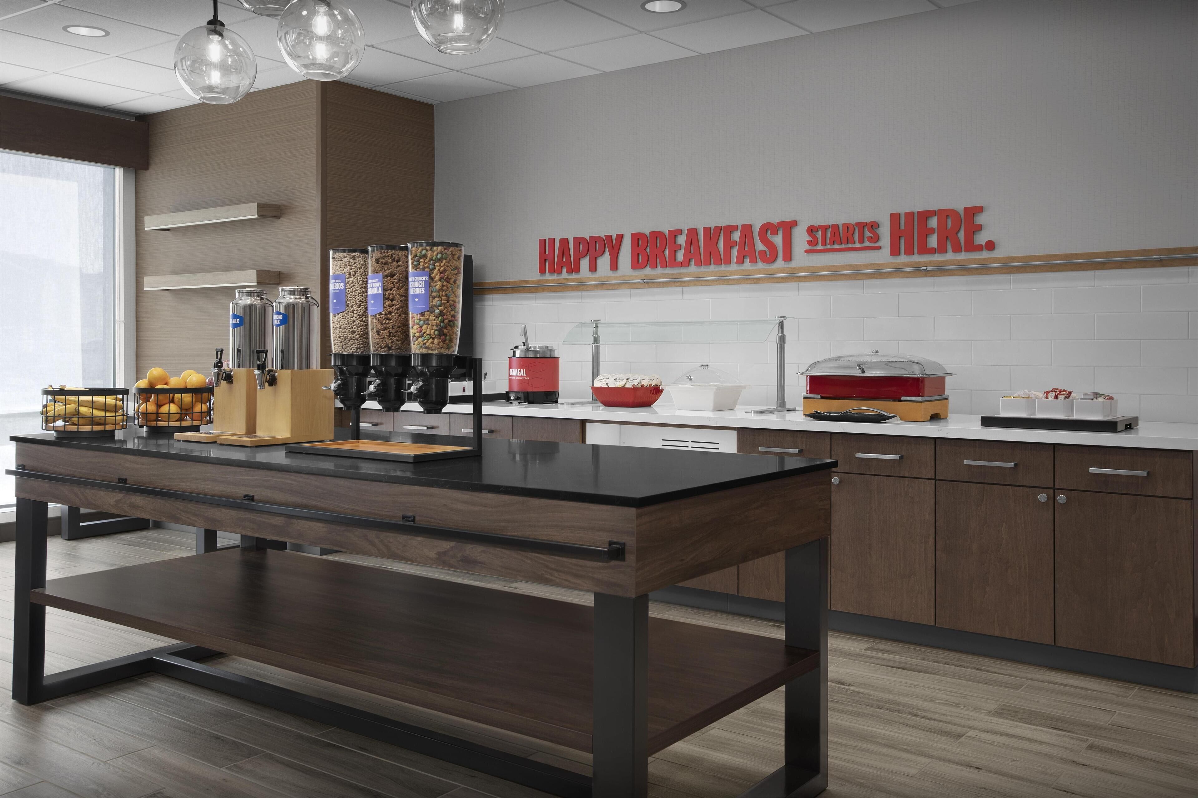 Uma área de café da manhã moderna, com uma mesa de madeira, máquinas de café e uma placa que diz "HAPPY BREAKFAST STARTS HERE".