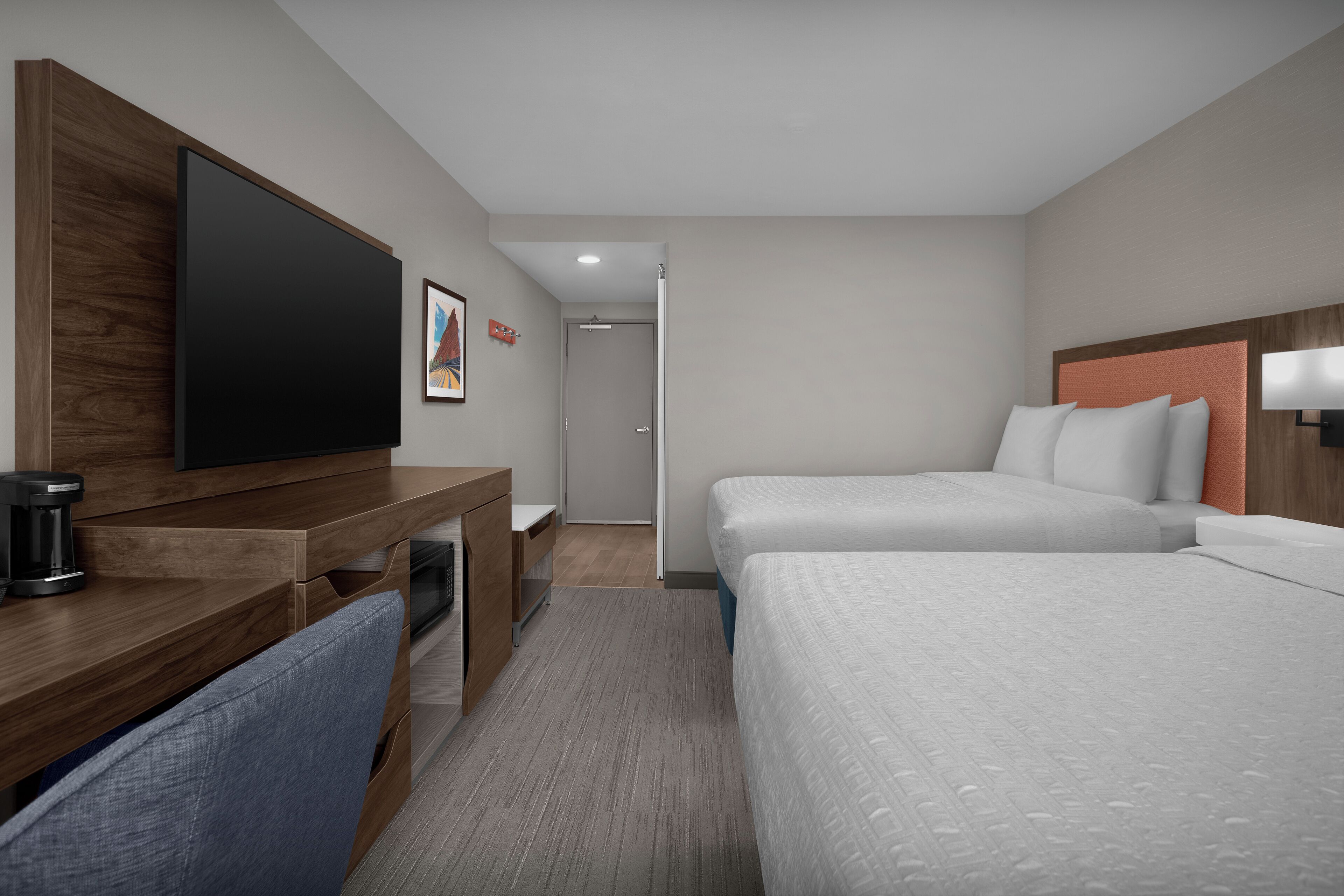 A hotel room with a wooden desk, a flat-screen TV, two beds with white bedding, a coffee maker, and a framed picture on the wall.
