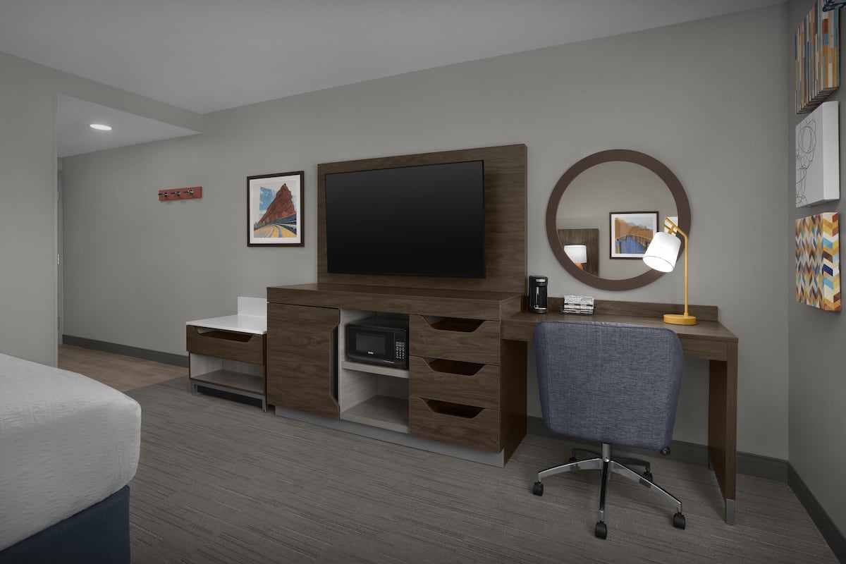 A hotel room with a wooden desk, a television, a microwave, a chair, and artwork on the walls.