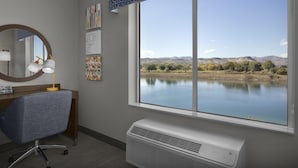 Een kamer met een groot raam, een bureau met stoel, een spiegel en een wandairconditioner.
