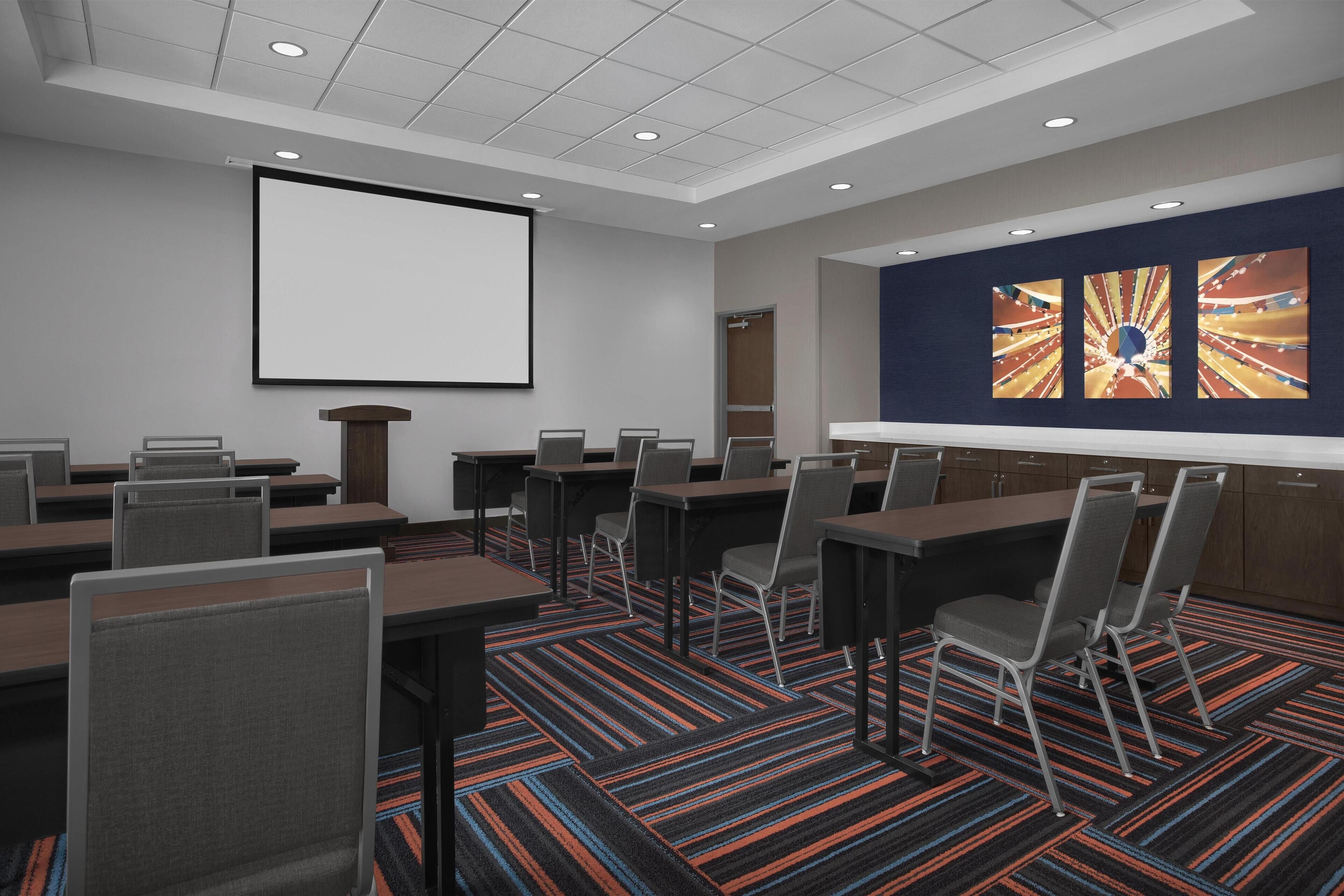 A conference room with a large screen, multiple tables, and chairs.