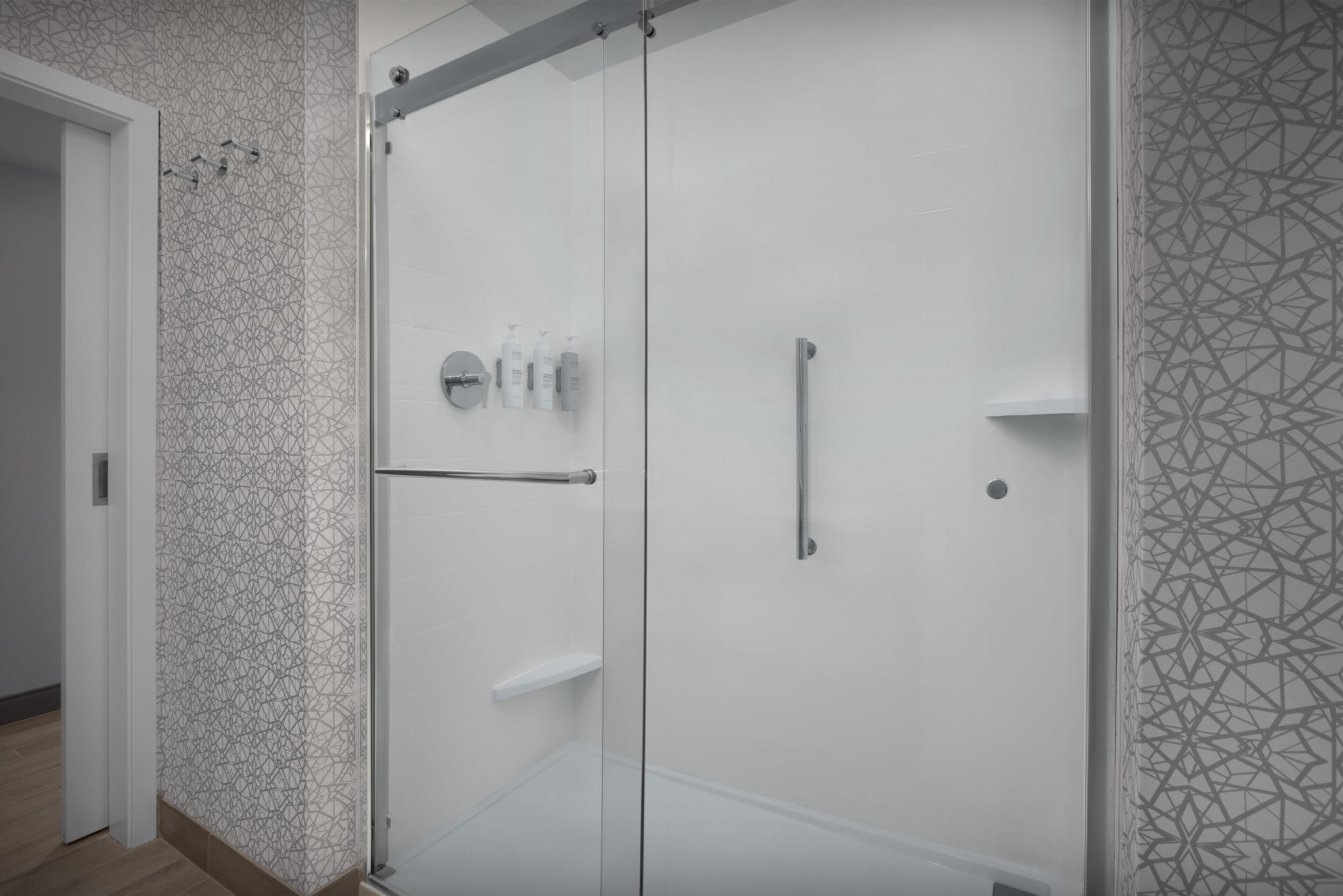 Ein modernes Badezimmer mit einer Duschkabine aus Glas, einer weißen Tür und einer Wand mit geometrischem Muster.