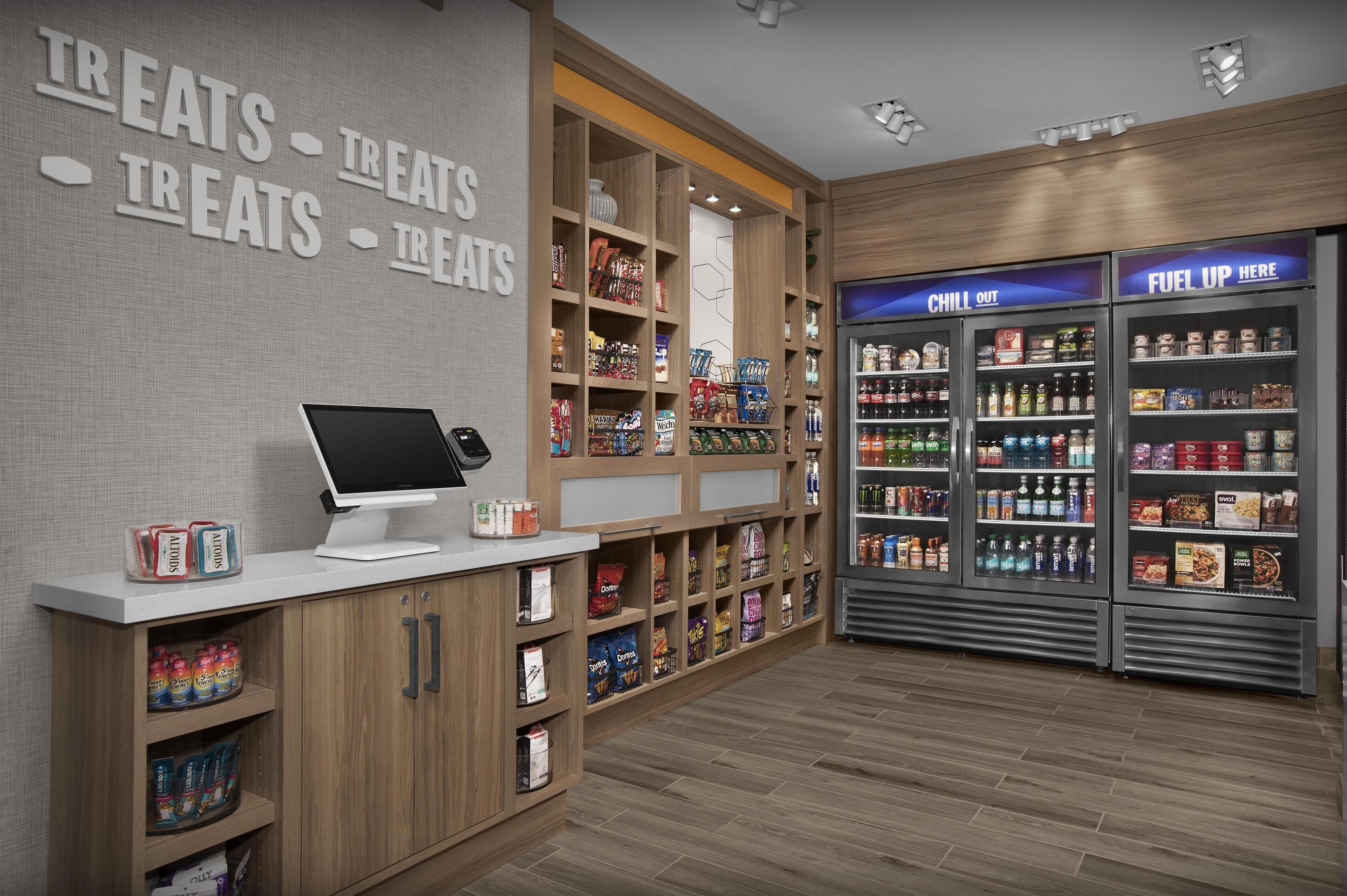Un bar à collations doté d’un distributeur en libre-service, d’étagères remplies de collations et de boissons, et de sections réfrigérées étiquetées « CHILI OUT » et « FAITES LE PLEIN ICI ».