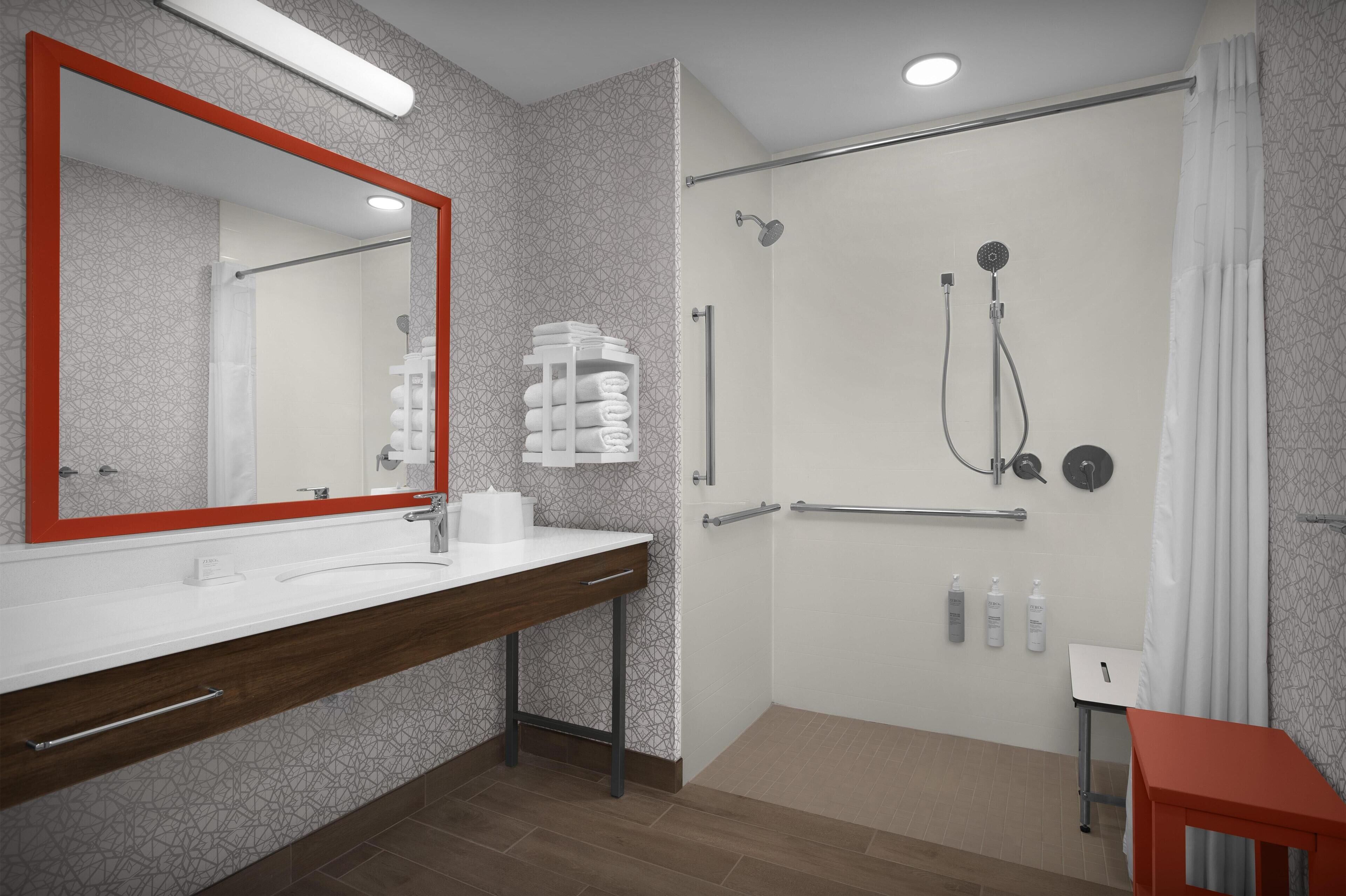 Un baño moderno con un espejo grande, zona de ducha y tocador con toallero.