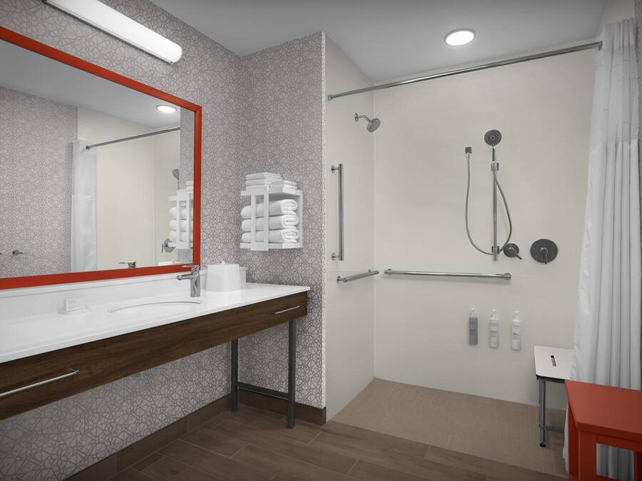 Un baño moderno con un espejo grande, zona de ducha y tocador con toallero.