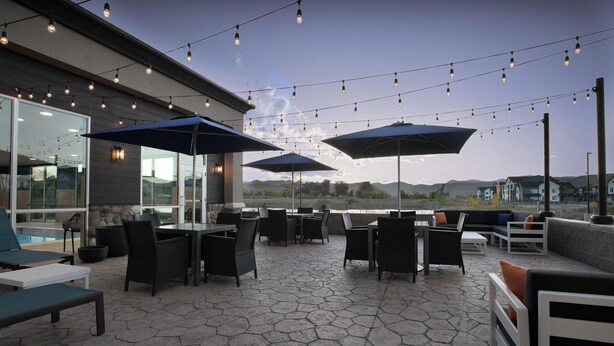 Een terras buiten met tafels, stoelen, lichtjes en parasols.