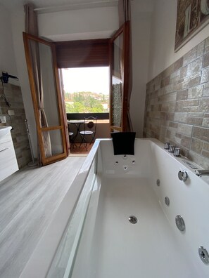 A modern bathroom with a large bathtub, a small table with chairs, and a view of buildings through an open door. - Perugia Suite B&B (Perugia)