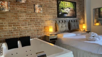 Ein Hotelzimmer mit Backsteinwand, einem großen Bett, einer Sitzecke mit Badewanne und Kunstwerken an der Wand.