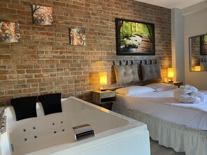A hotel room with a brick wall, a large bed, a sitting area with a bathtub, and artwork on the wall. - Perugia Suite B&B (Perugia)