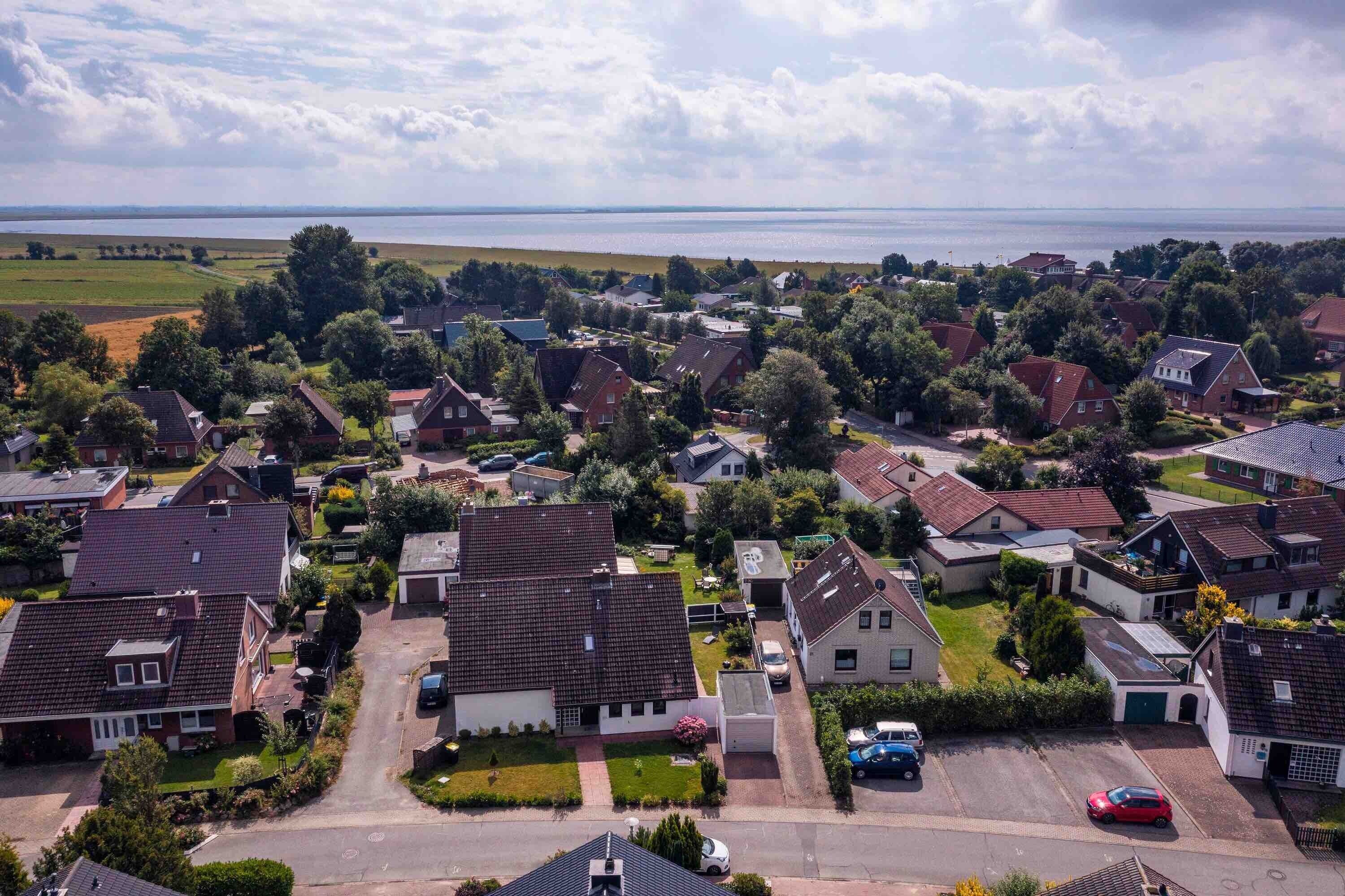 Eine Luftaufnahme eines Wohngebiets mit Häusern, einer Straße und einem Gewässer im Hintergrund.