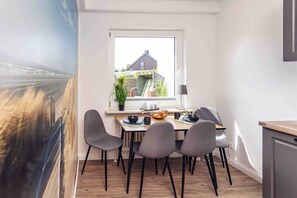 Un espace repas comprenant une table, des chaises, une fenêtre et donnant sur une maison.